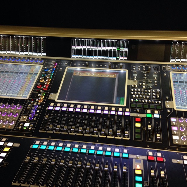 Close-up of a professional audio mixing console featuring various knobs, sliders, and digital screens for sound control.